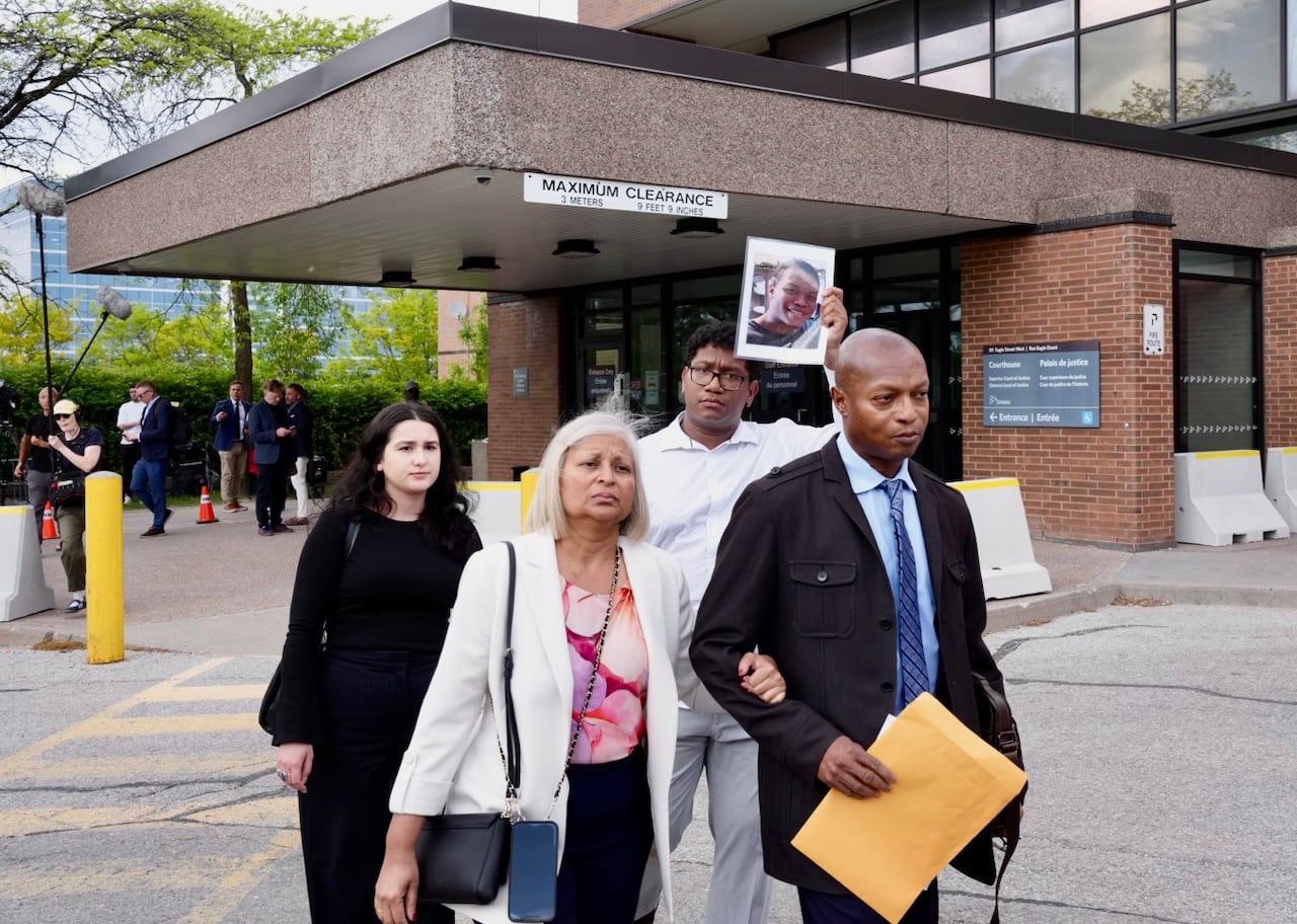 A group of people armed linked walking outside a courthouse. One is holding up a photo of a person who died.