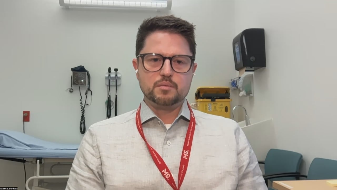 A man sits in a clinic room, with a patient table behind him.