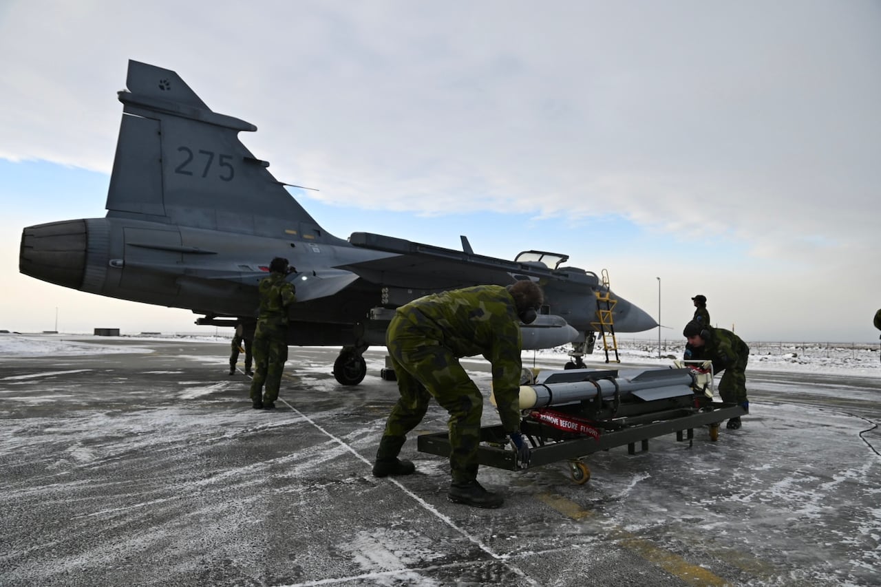Two men in unifrom wheel a missle towad a fighter jet.