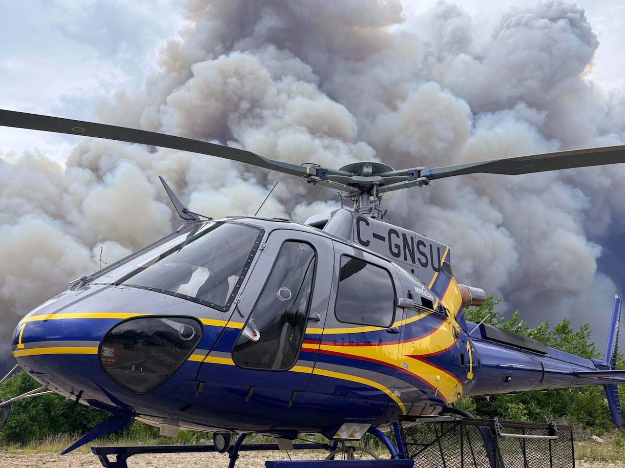 A helicopter parks against the backdrop of thick smoke of a wildfire