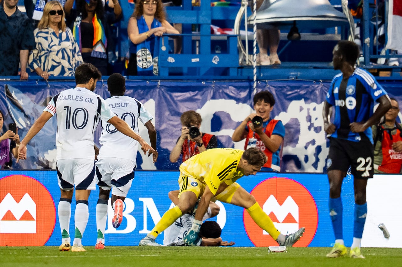 A soccer goalkeeper is standing over another player on the ground.