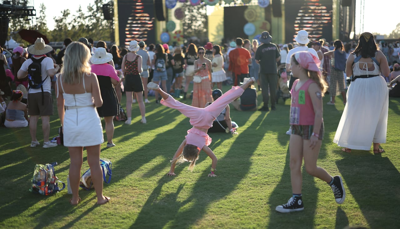 A girl performs a cartwheel on the grass at an outdoor music festival.