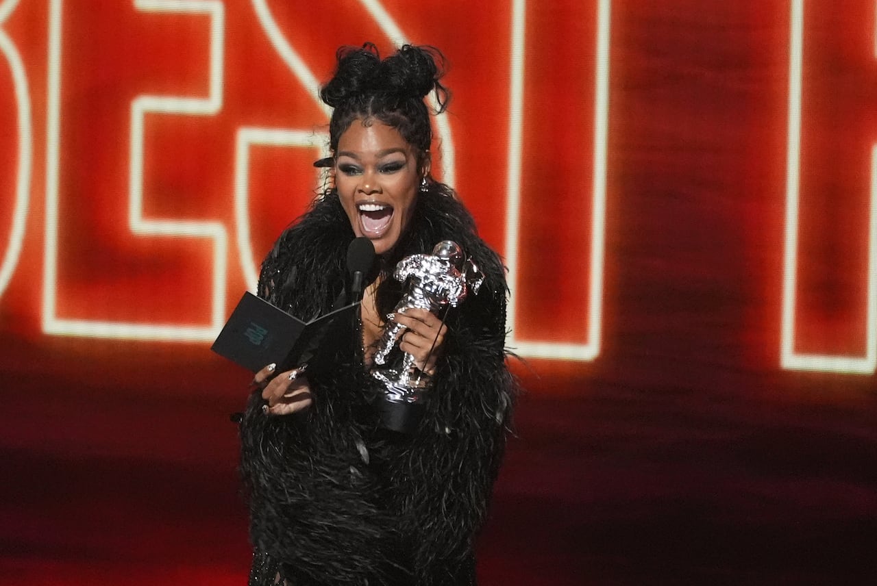 A woman holding a black envelope that says "Pop" and a silver statuette smiles wildly on a stage with a bright red/orange backdrop.