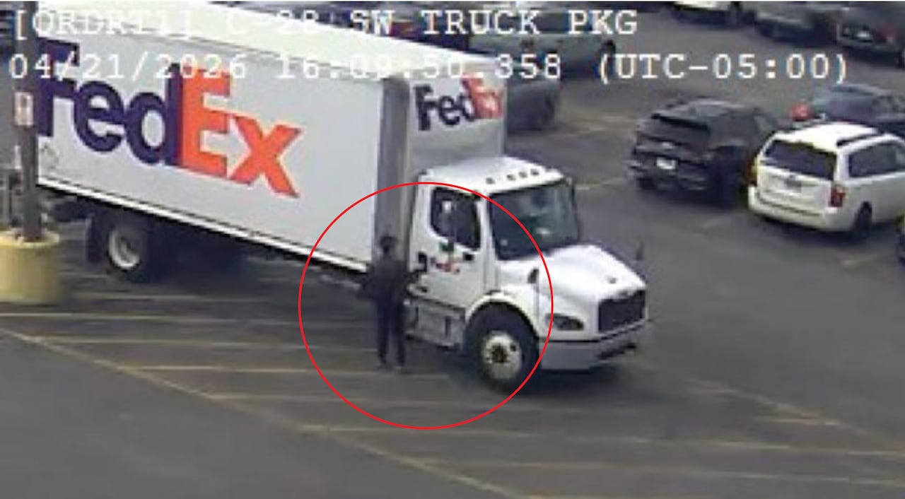 A man in dark clothes stands next to a white FedEx truck.