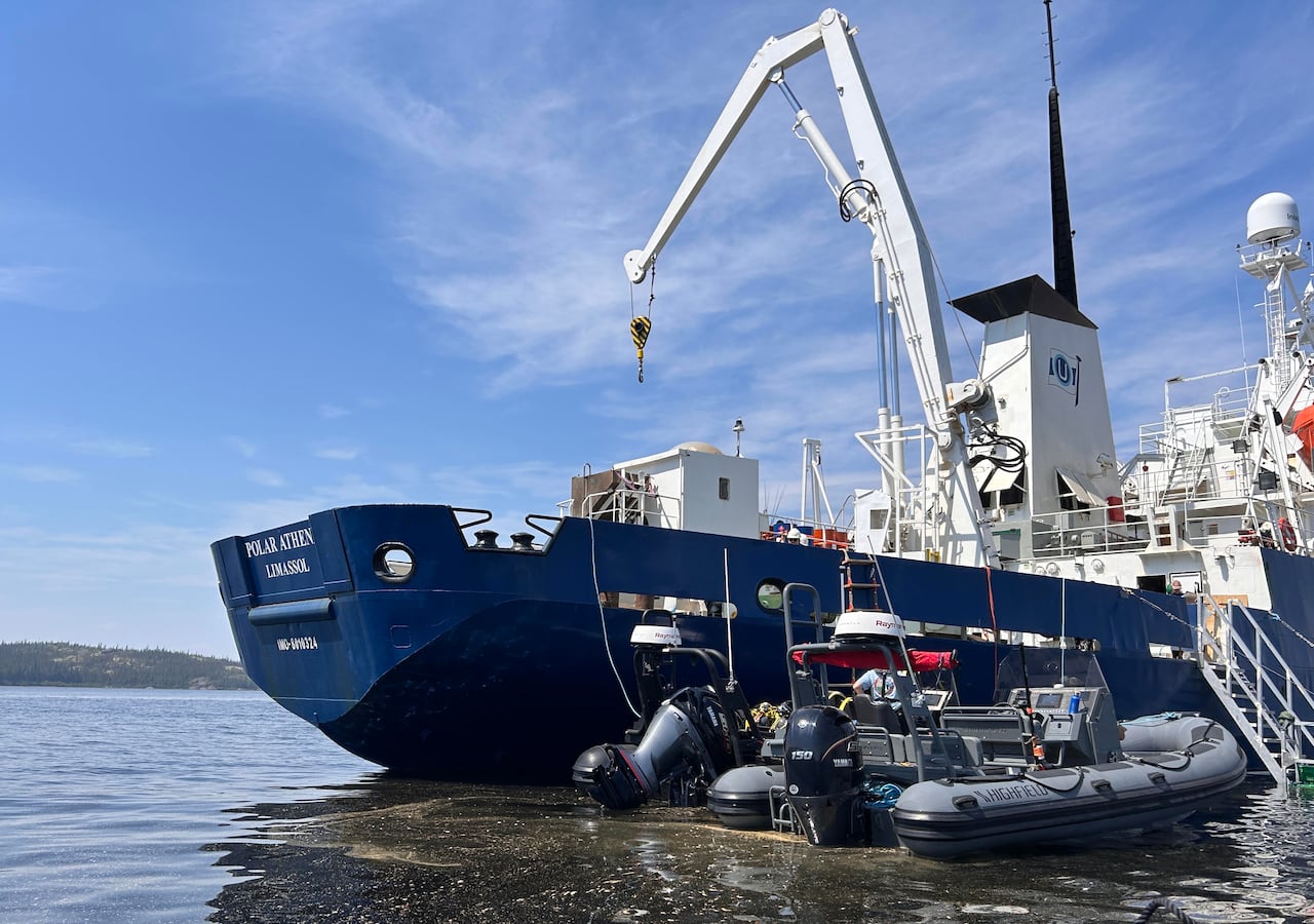 A large blue and white expedition vessel is docked in the harbour, next to a couple of smaller Zodiac boats.