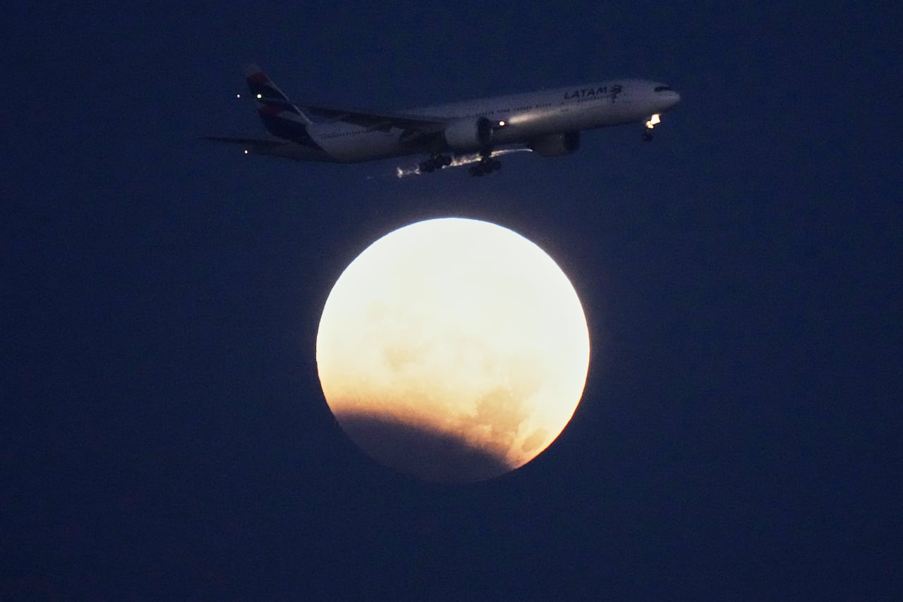 A plane passing a full moon during a partial lunar eclipse in the sky.