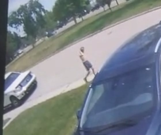 A still from CCTV footage showing a shirtless boy walking on a sidewalk.