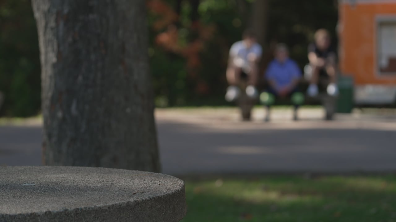 People are sitting on a bench in the background, their bodies and faces blurred.