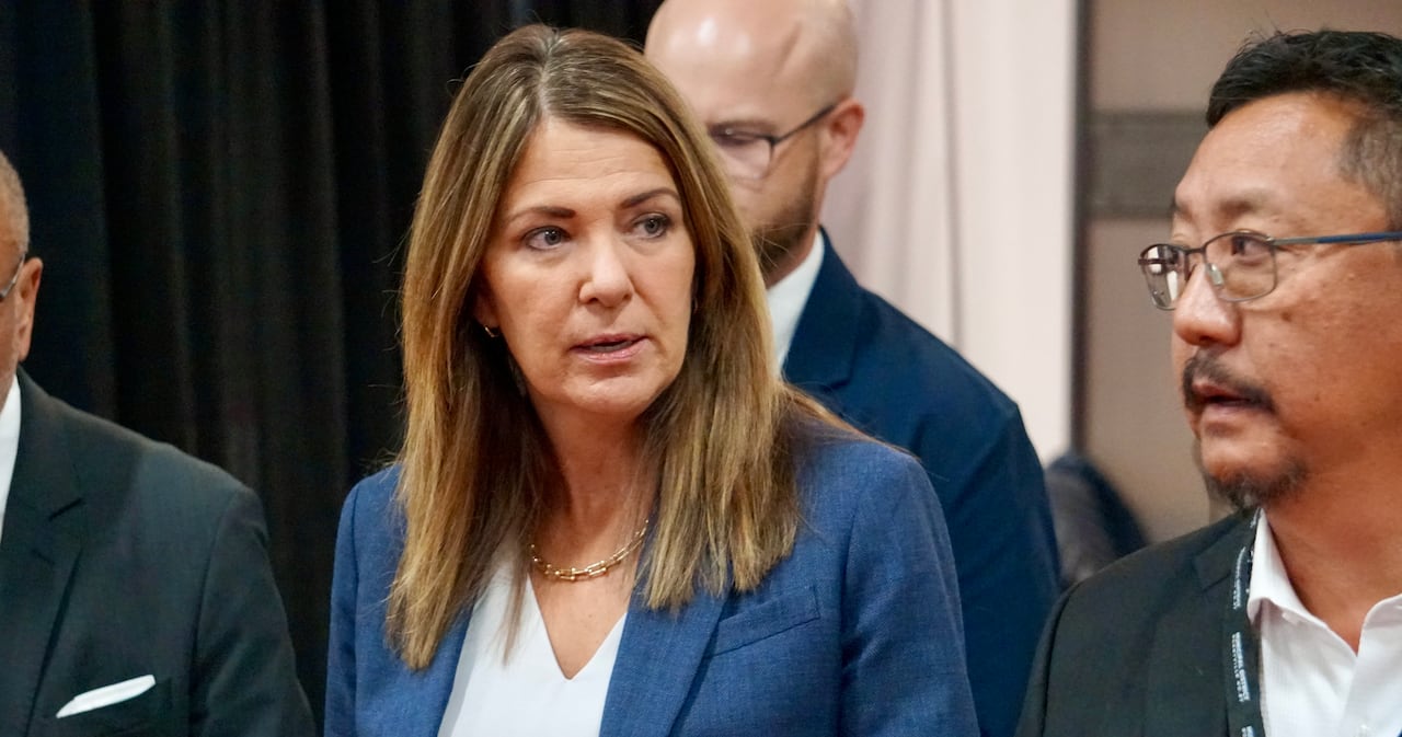 The premier walks into a room with people in suits walking beside her.