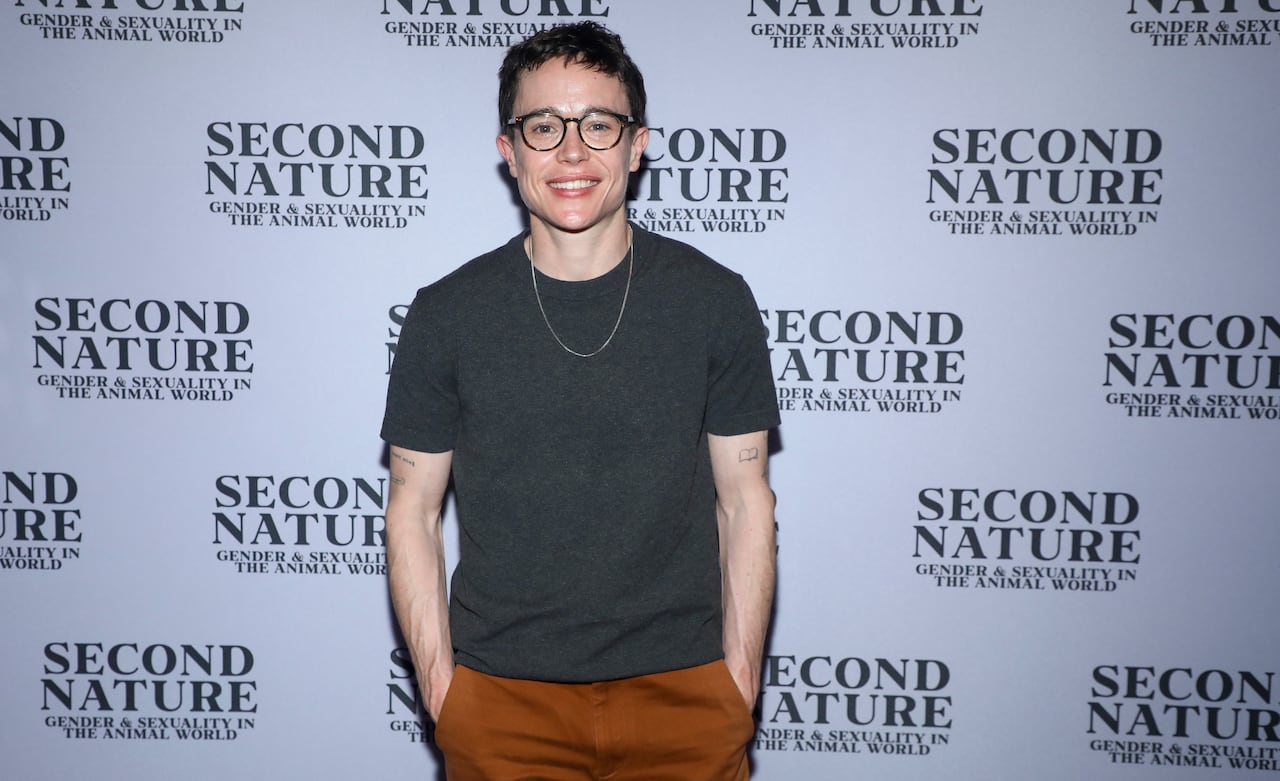 A man stands with his hands in his pockets, smiling.