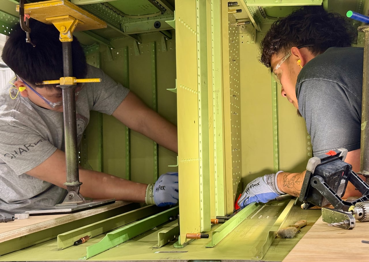 Two workers are shown inside of a steel wing.