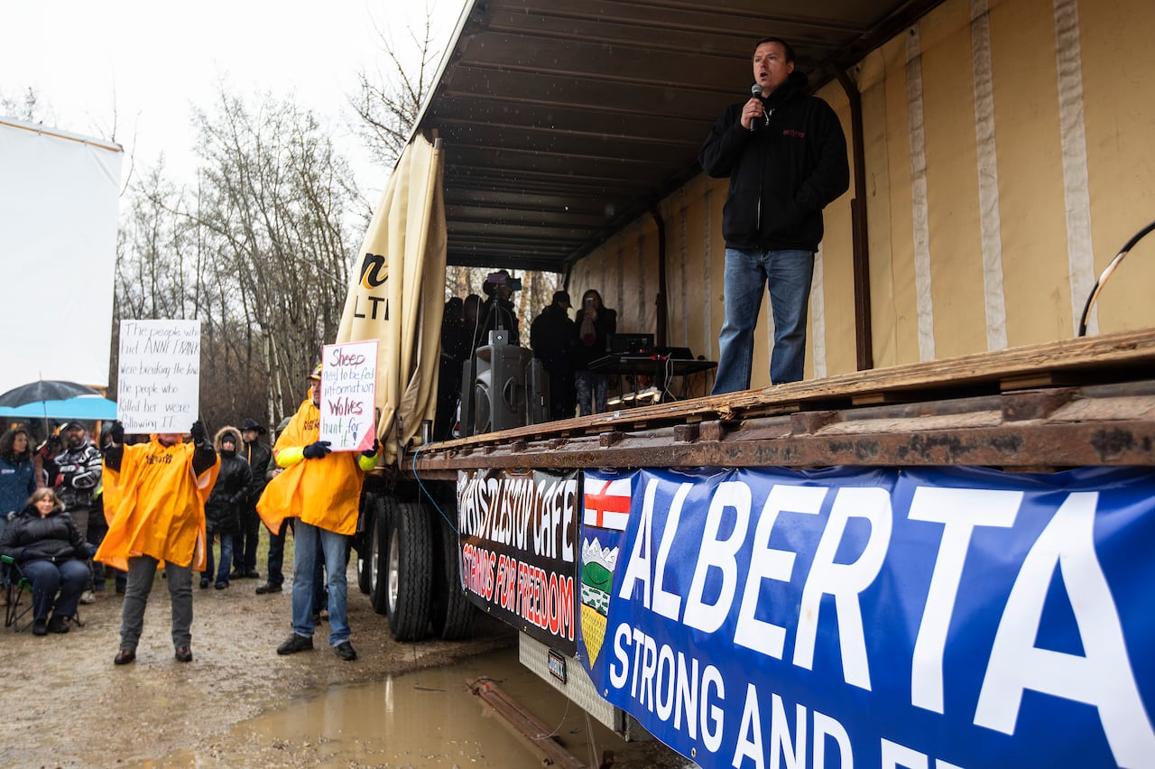 Man speaks on stage at protest, with large "Alberta strong and free" banner beneath him.