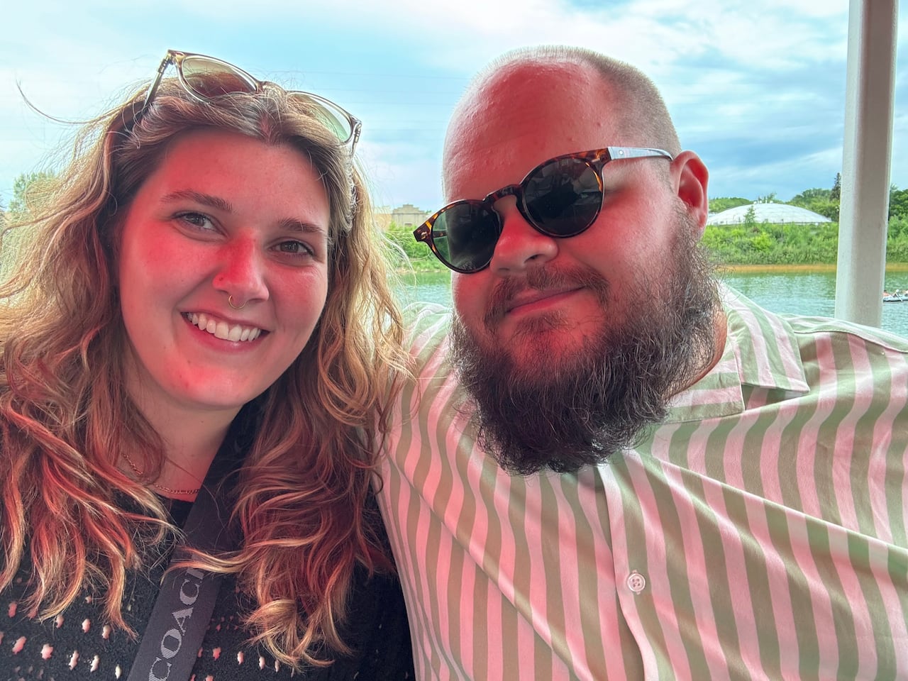 a man and a woman pose together with a body of water behind them