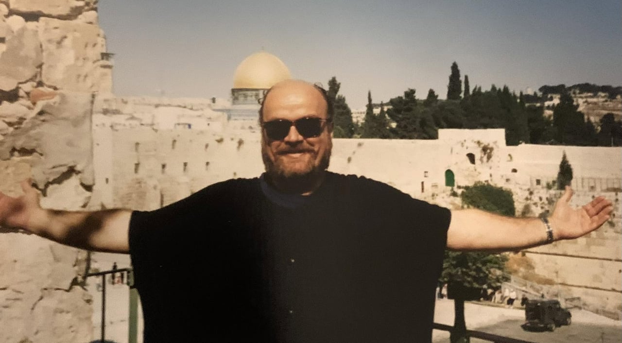 A person in a large black garment stands in front of a stone structure