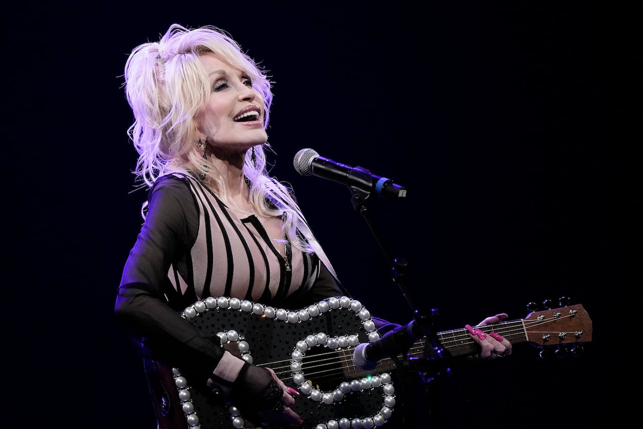 A woman holds a guitar and sings on stage