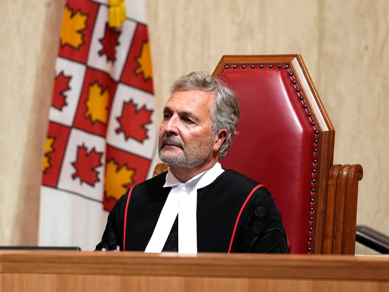 A man in a robe sitting behind a microphone on a red chair.