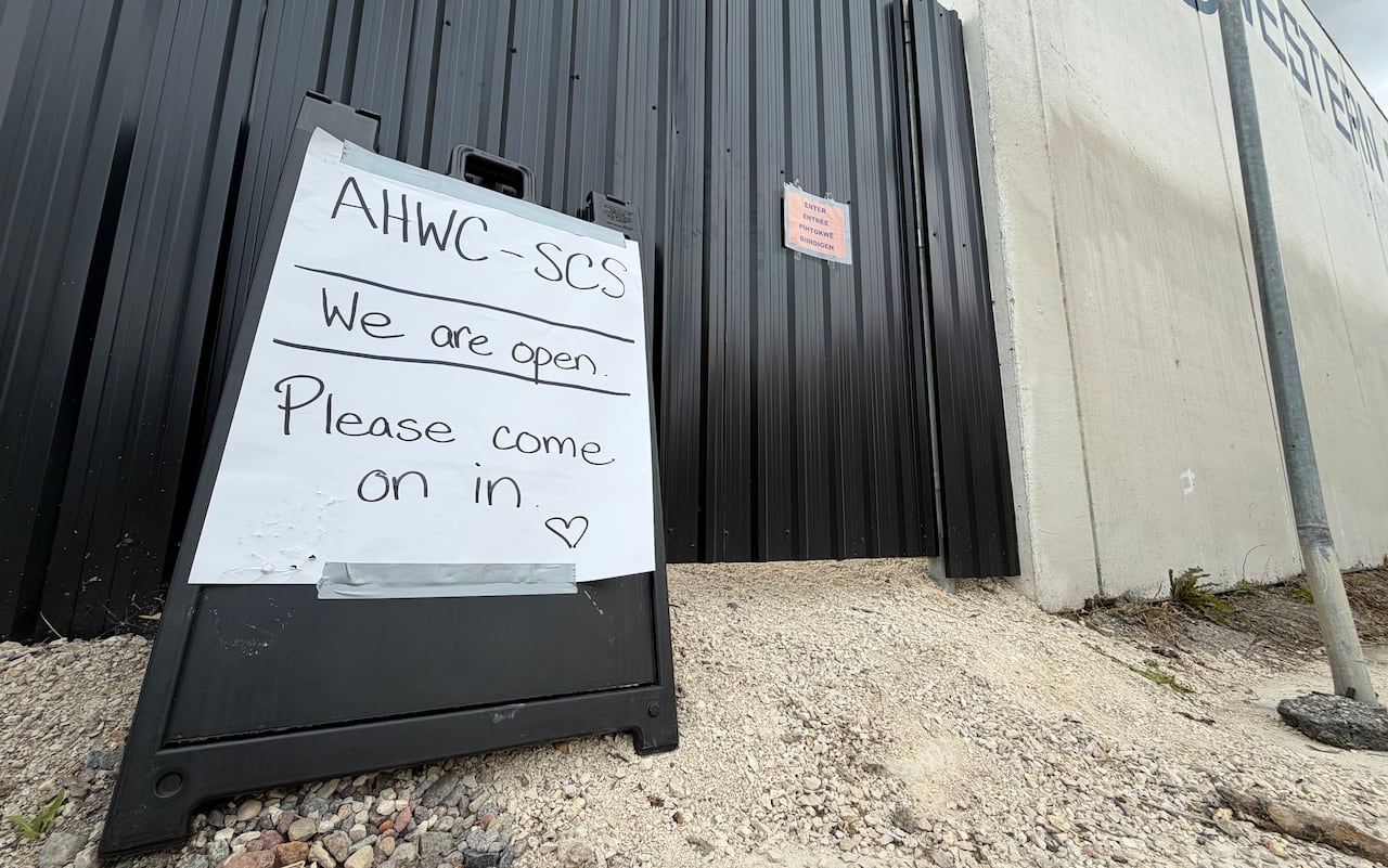 A sign that says 'we're open. lease come in' outside an industrial building