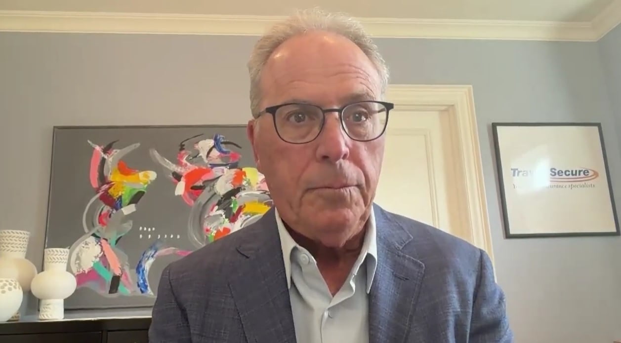 A man in glasses and a blazer sits in his home office on a video call.