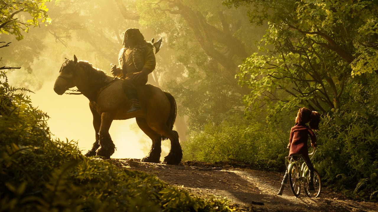 A stop-motion animation image shows a girl on a bike in front of a silhouette of a large man on a horse. They are in a forest.
