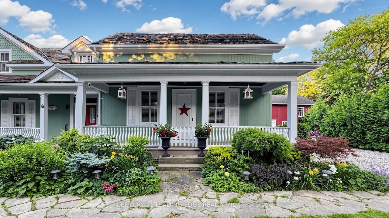A green house with a white porch, well-manicured garden, and a red star on the front door.