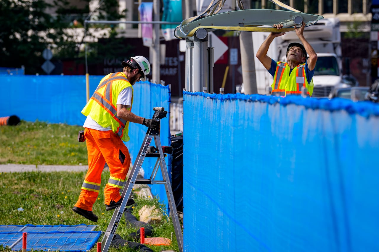 Construction workers in orange vests are seen working outdoors.