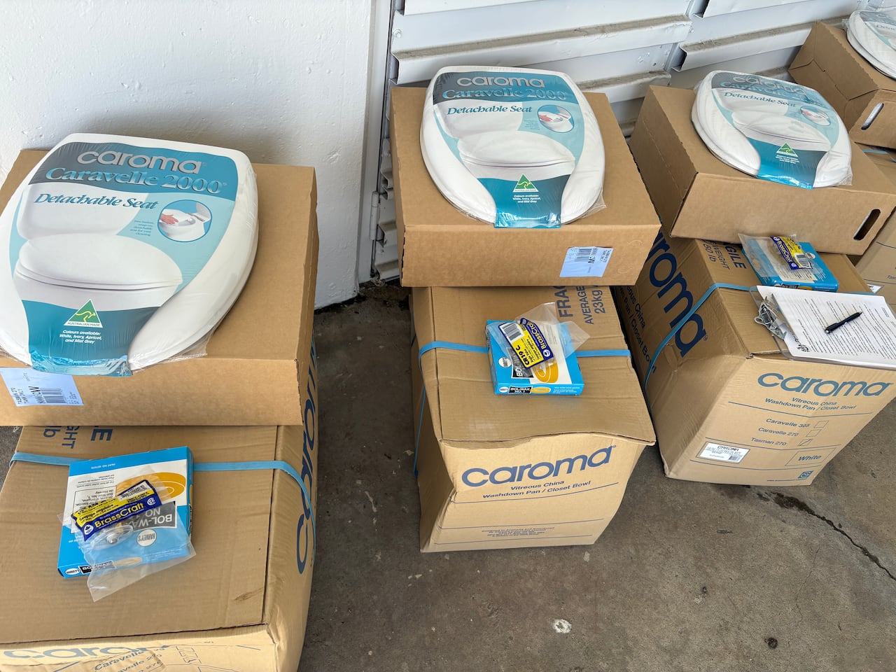 Cardboard boxes with toilet seats in plastic wrap are lined up against a building.