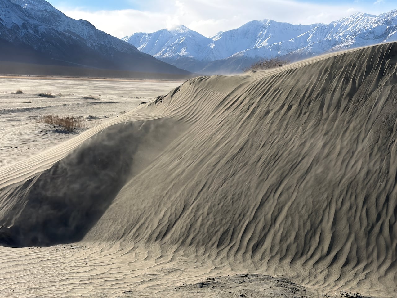 Wind-sculpted grey sediment forms a steep ridge on the floor of the Ä'äy Chù Valley, with snowy mountains in the background.