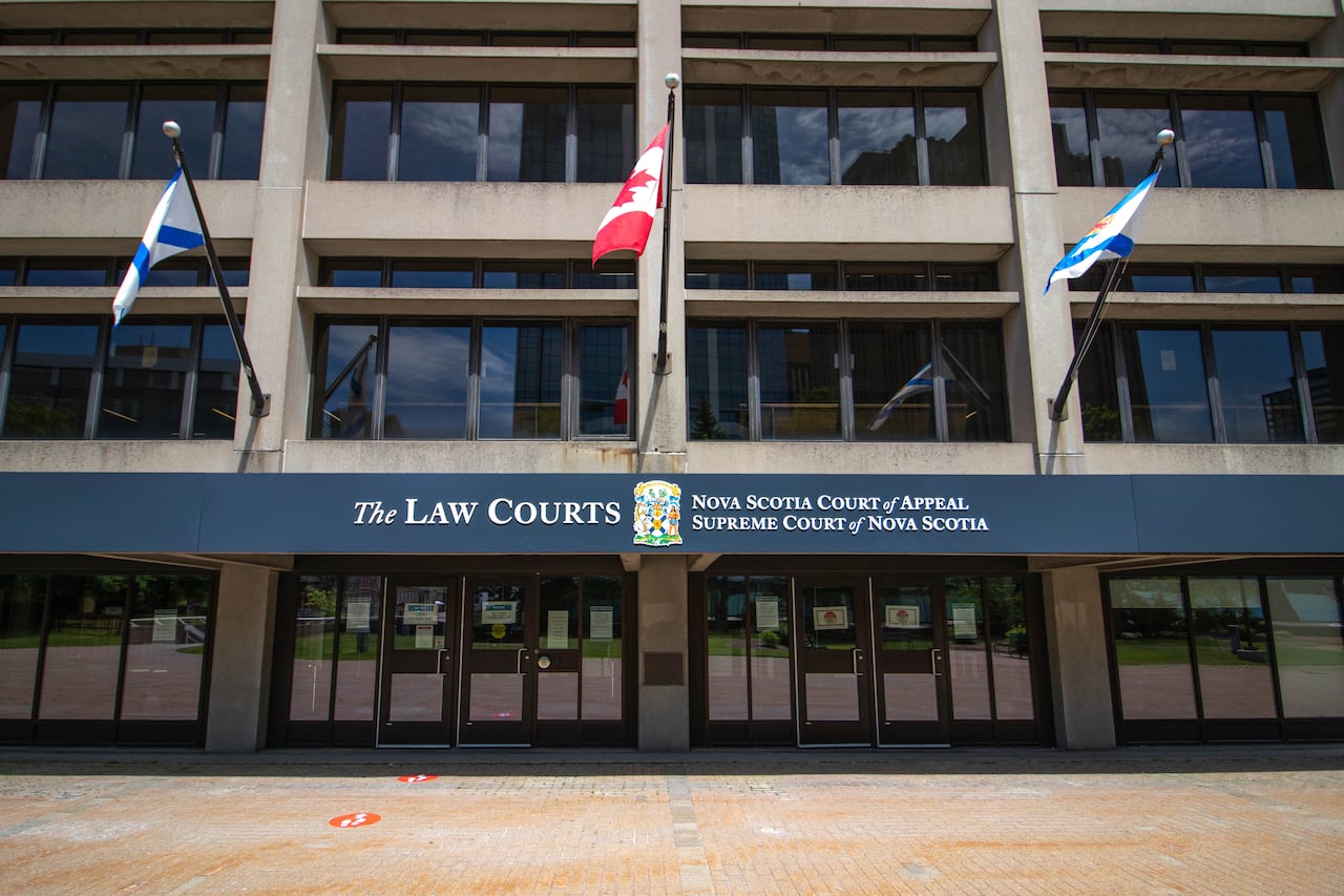 A Canadian flag and two others flutter outside of an austere court building. 