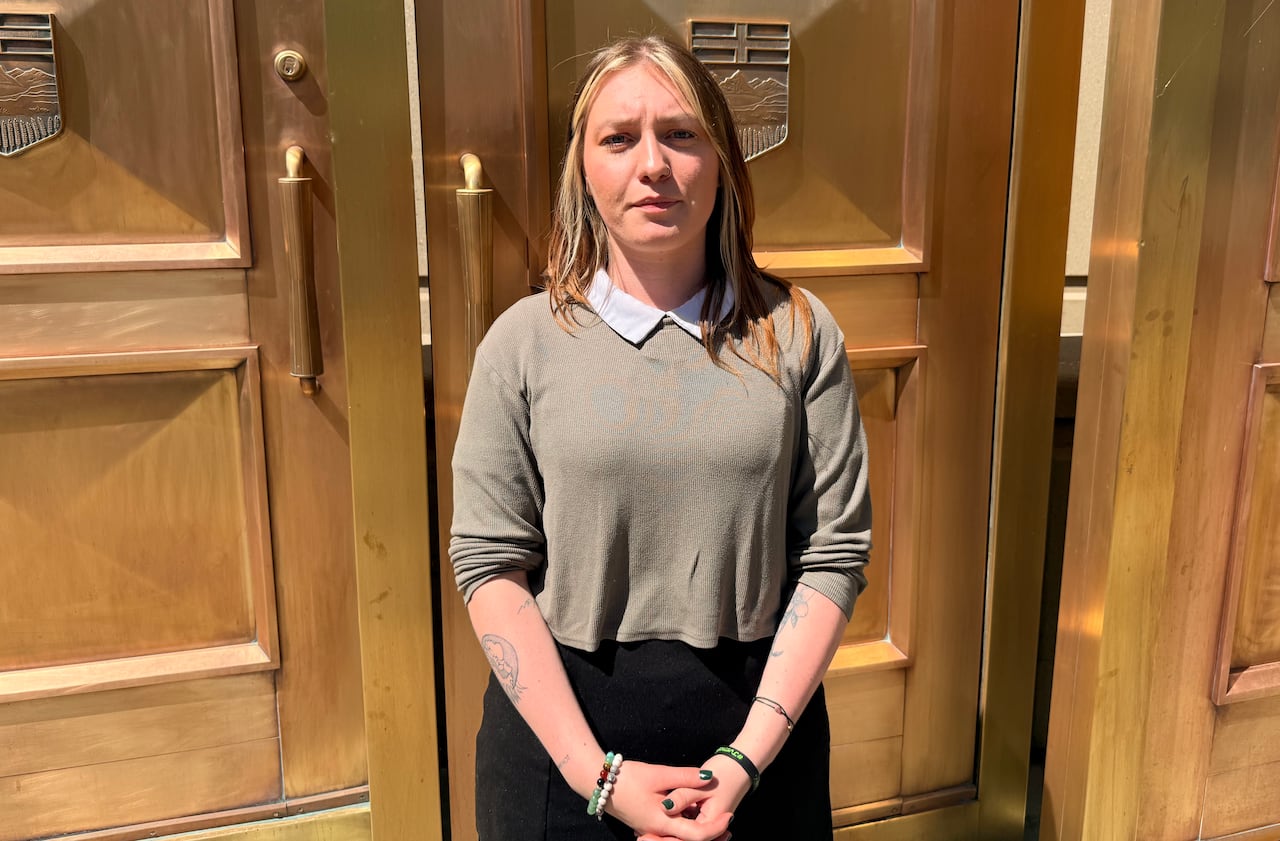 A young woman stands in front of gold courthouse doors.