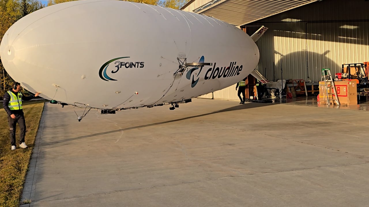 Two flight crew members carrying an airship from a hangar.