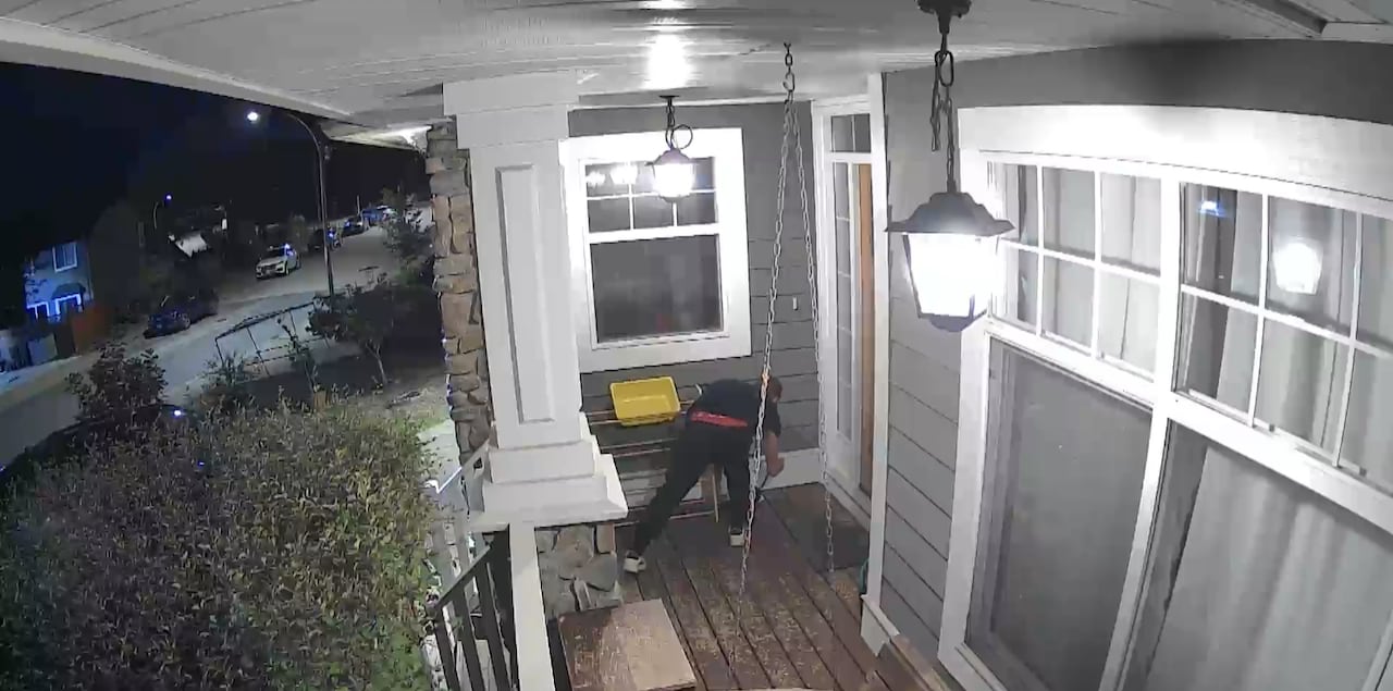 A man crouches next to a wall socket on a porch of a home in CCTV footage.