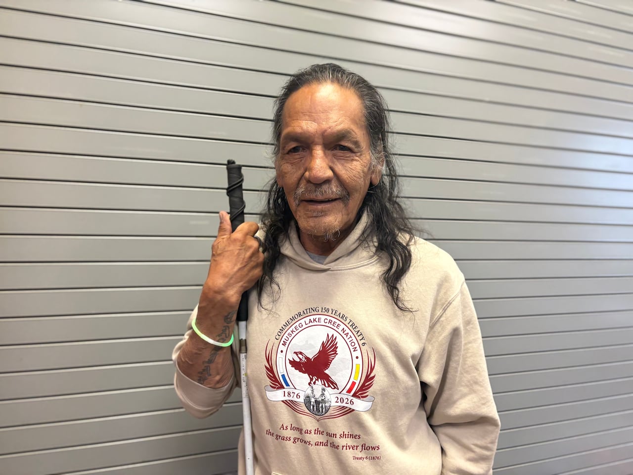 A man in a hoodie smiles at the camera while holding a walking cane.