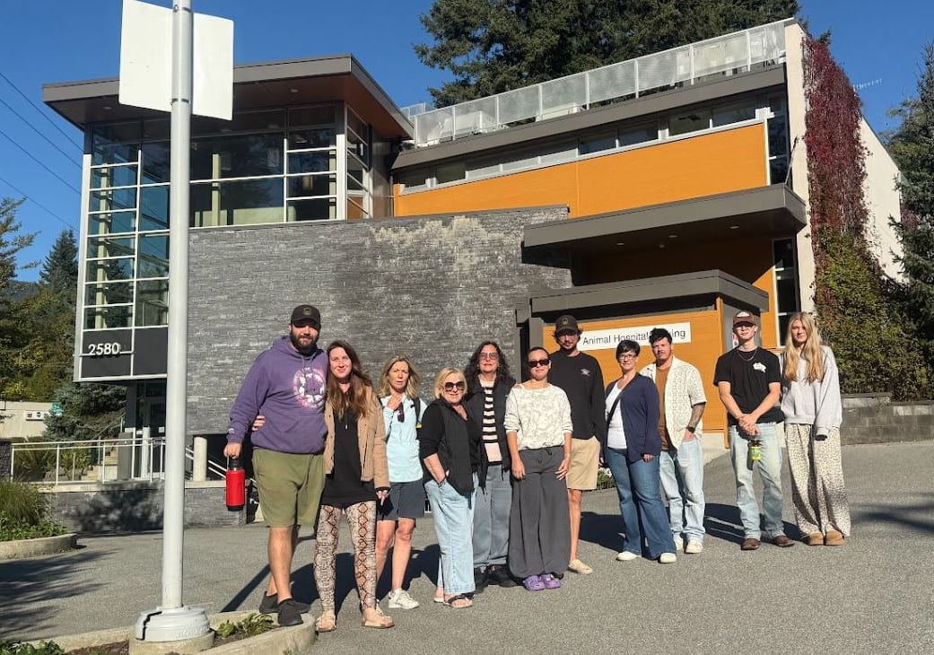A group of 11 people stand outside a large building.