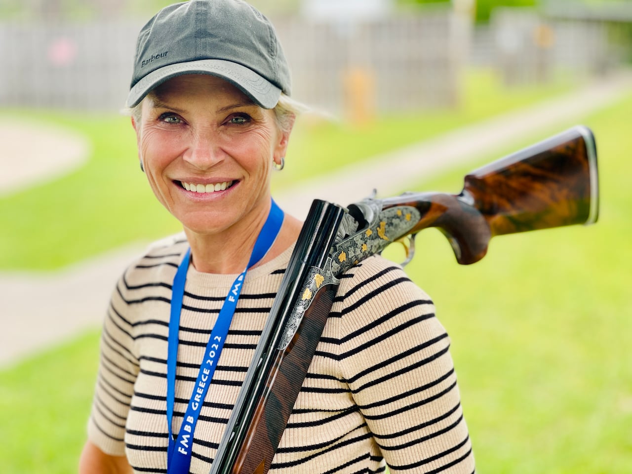 Leigh Bianco, wearing a baseball cap and smiling, with a shotgun resting on her shoulder.