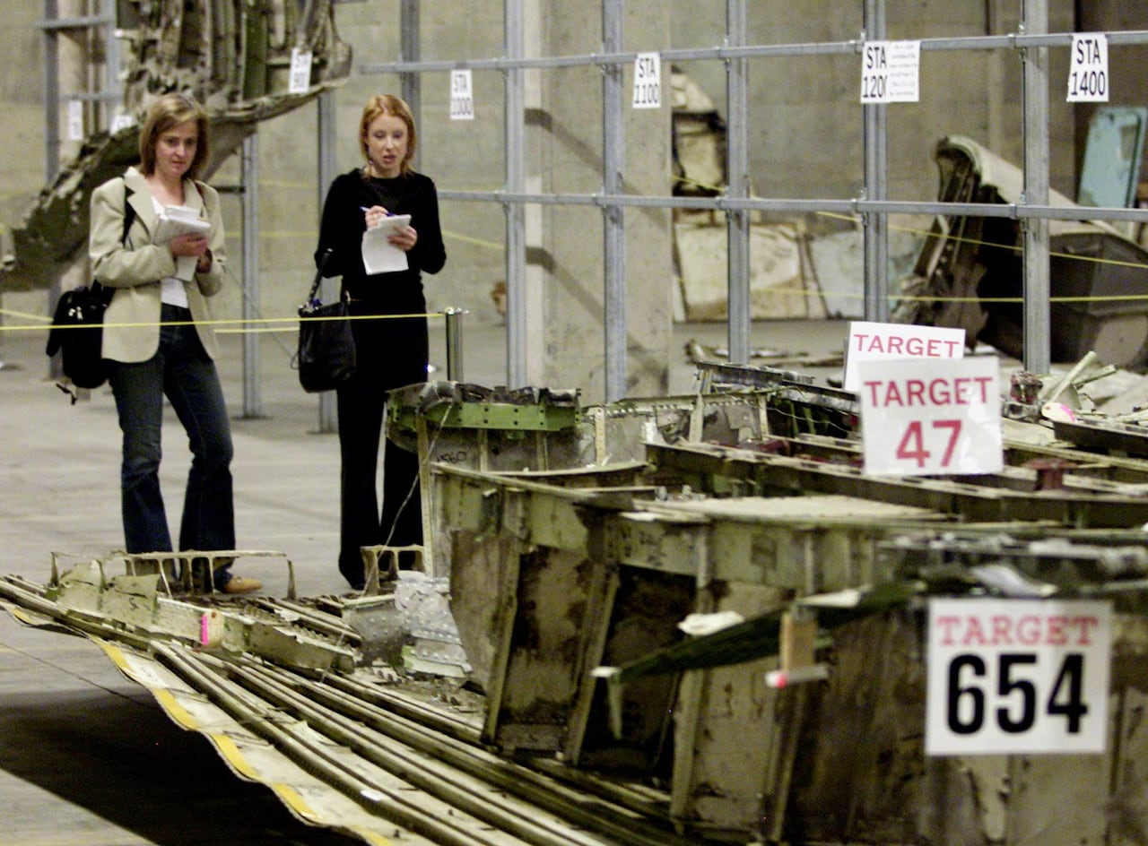 People stand over wreckage in a warehouse, taking notes