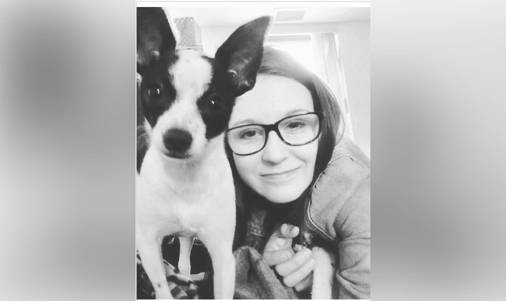 A woman with long hair and glasses with her small dog.