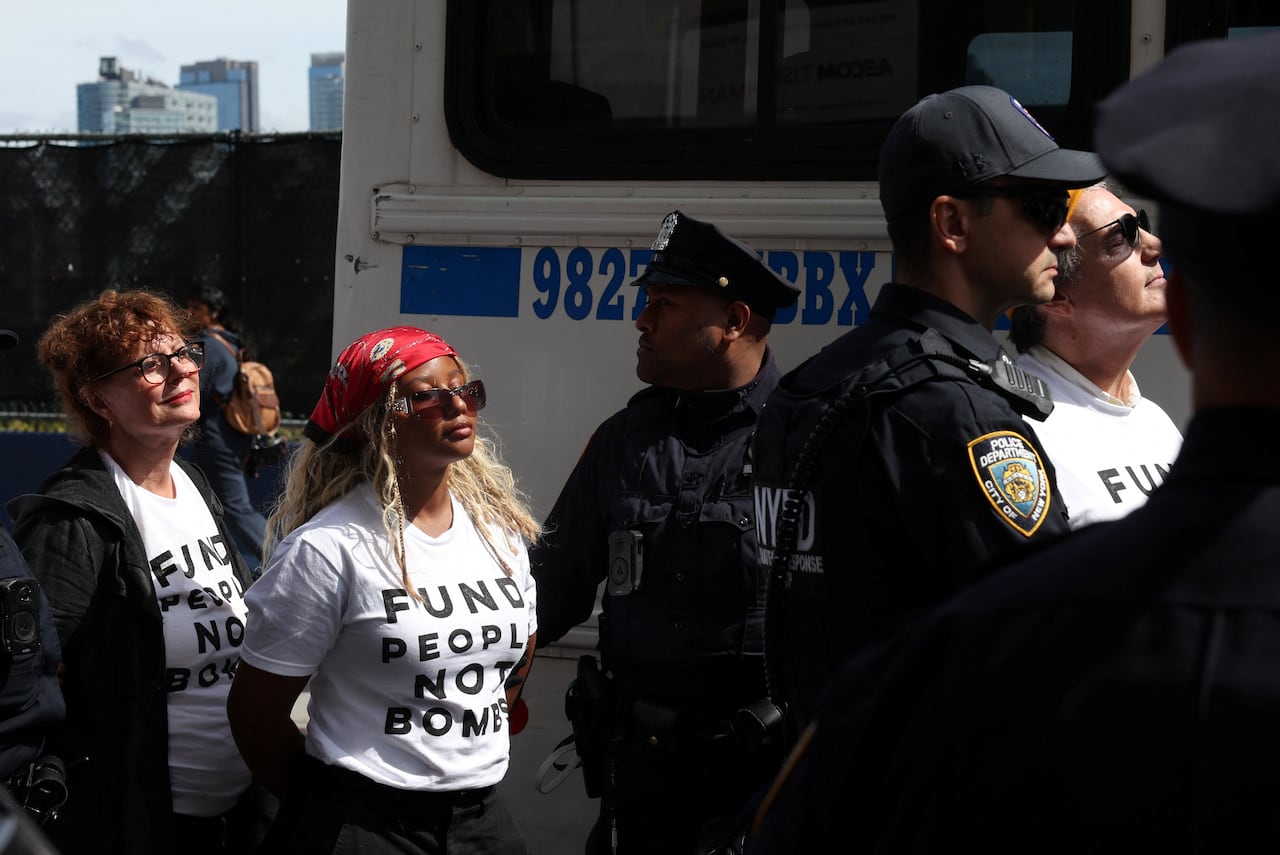 Women wearing shirts that say "fund people not bombs" are detained by police.