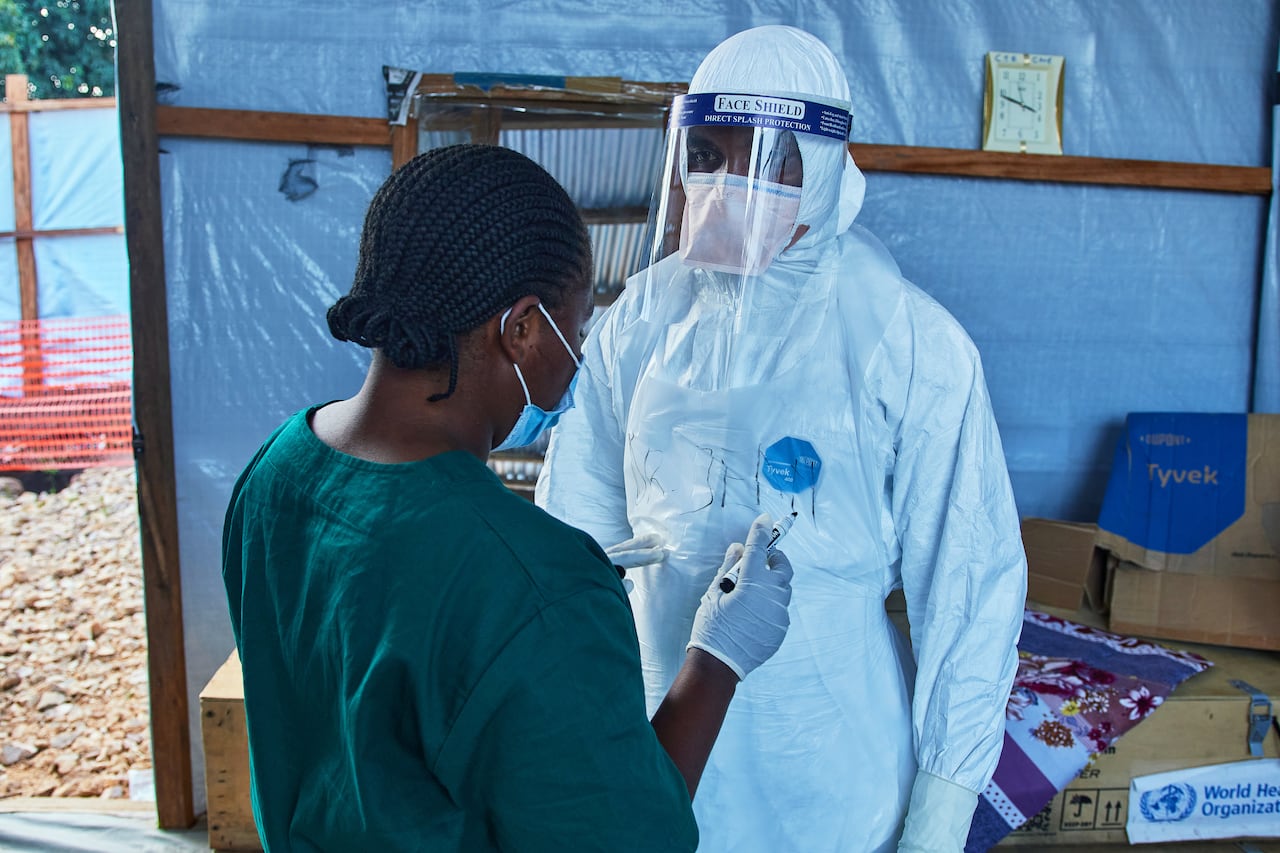 Two health-care workers, one wearing a full body protection suit including a face shield, are seen in a makeshift tent.