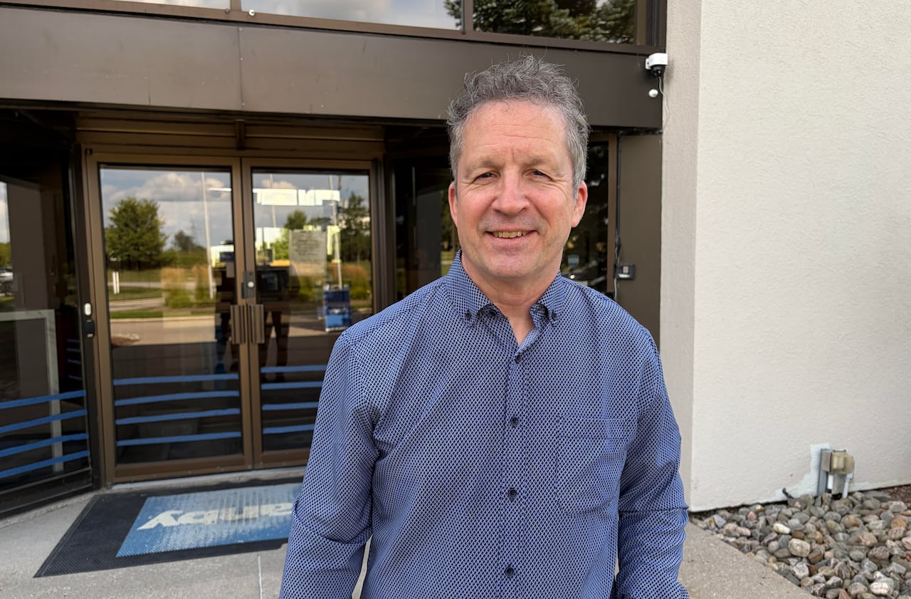 a man in a blue collared shirt stands in front of the glass doors of a building