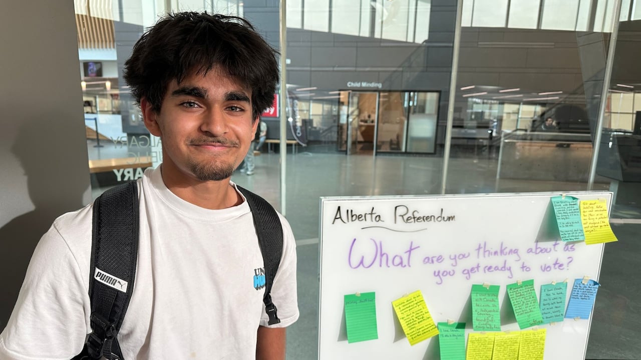 A young man grins at the camera beside a whiteboard.
