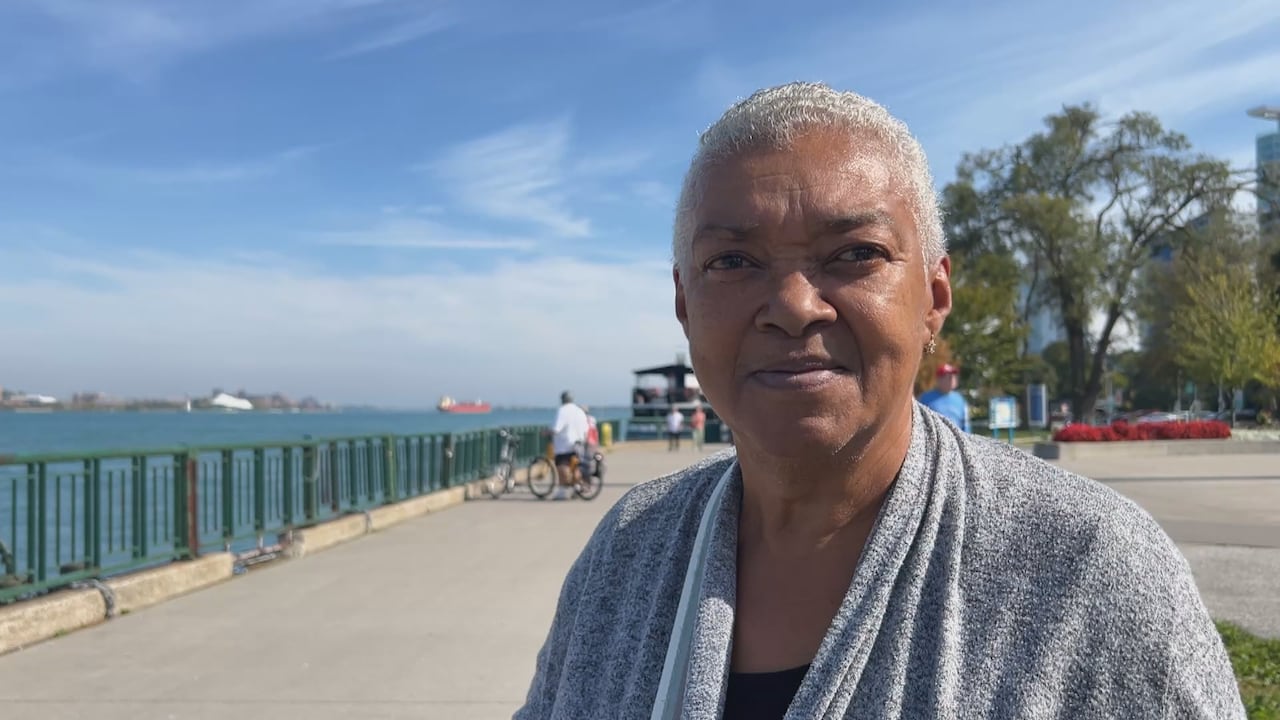 A woman stands next to the Detroit River.