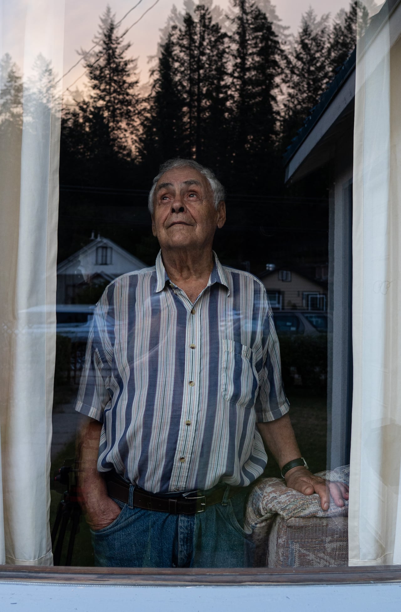 An elderly man in a short-sleeve button-down and jeans gazes upward.