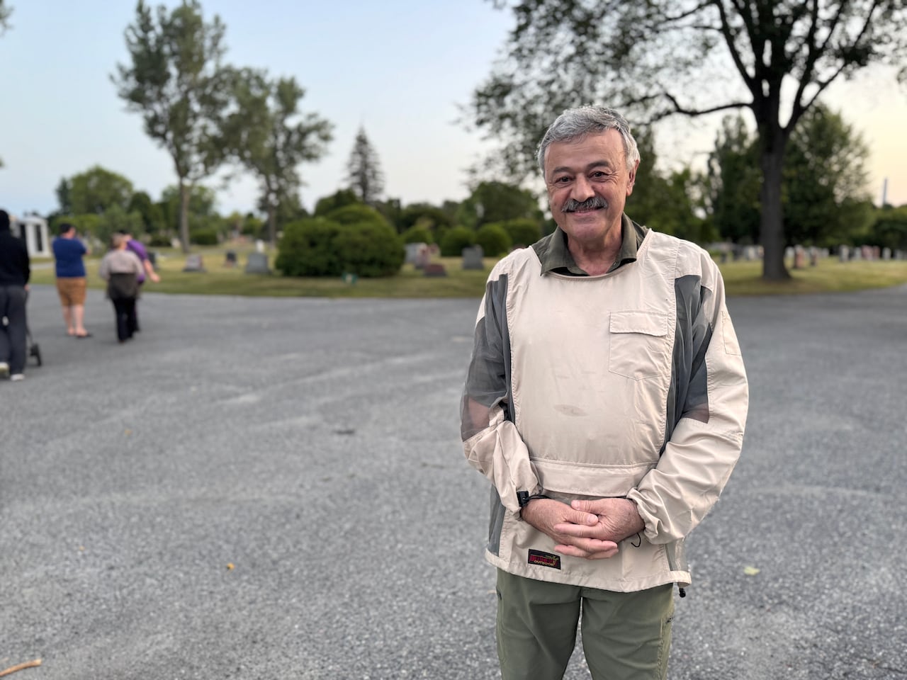 A man with gray hair stands similing while wearing a mosquito jacket.
