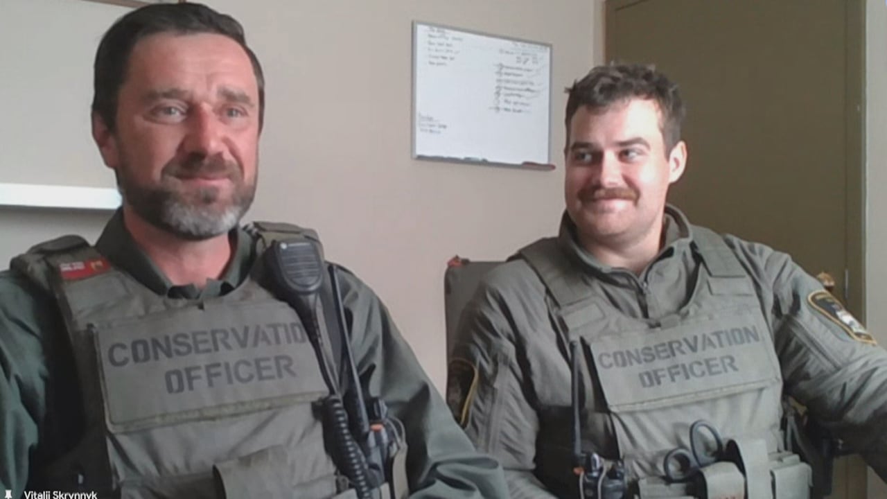 Two men in Conservation officer uniforms sit side by side