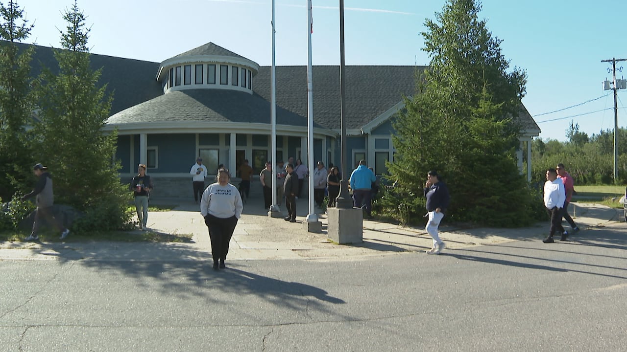 More than a dozen people stand outside a multi-purpose building with flags out front.
