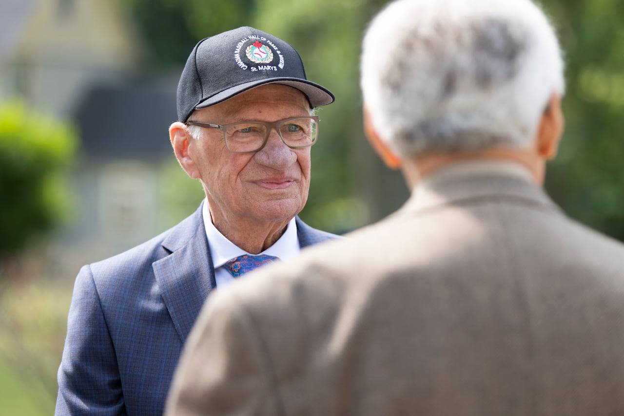 A man in a baseball cap looks past another person and smiles at camera.