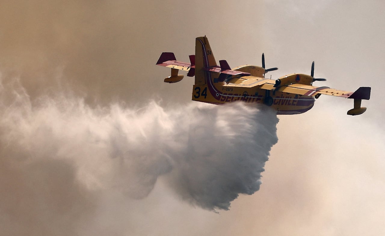 The plane drops water while flying in a smoky sky.