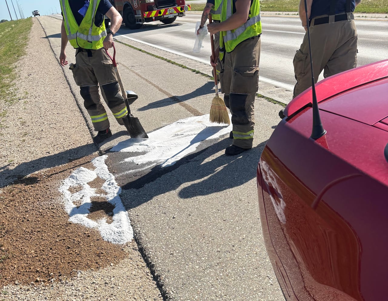 Three people from a fire department work to clean up a gas leak from a car on a highway.