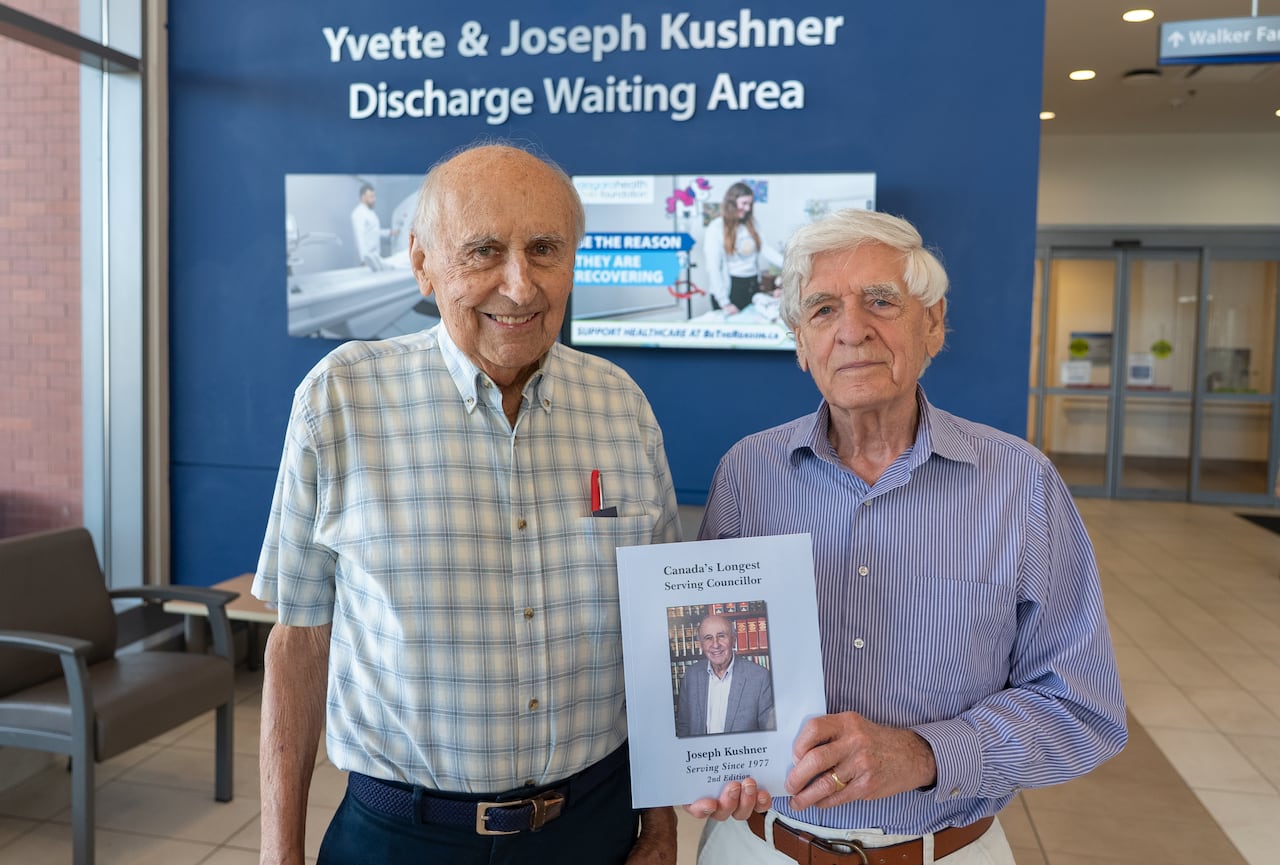 portrait of two men holding a book at a hospital waiting area