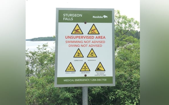 A sign warns against dangers at a location near water.